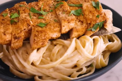 Tossing fettuccine pasta with creamy Alfredo sauce and sliced pan-seared chicken breasts