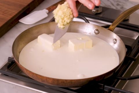 Whisking heavy cream, butter, garlic, and freshly grated parmesan cheese for Alfredo sauce