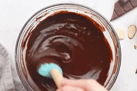 Pouring melted chocolate over the cake and adding sliced almonds around the top perimeter
