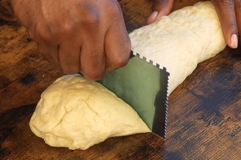 Portioning and cutting the rolled dinner roll dough into rolls using a bench scraper