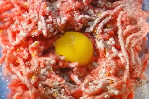 Adding egg yolk and seasoning blend to ground beef patty